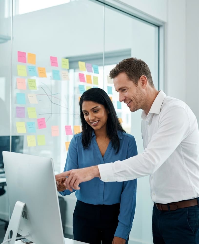 Dupla de vendedores analisando o funil no monitor com post-its ao fundo